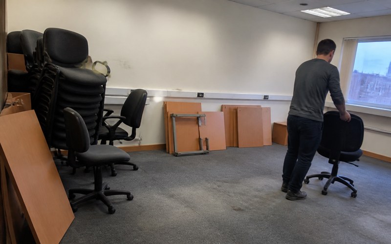Stacked office chairs and dismantled desk tops in an emptied office