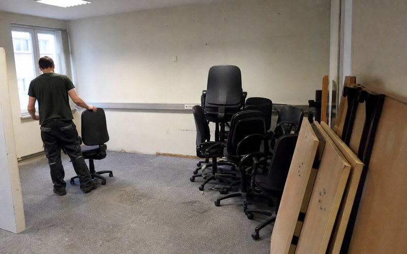 Stacked office chairs and table tops leaning against a wall in an emptied room