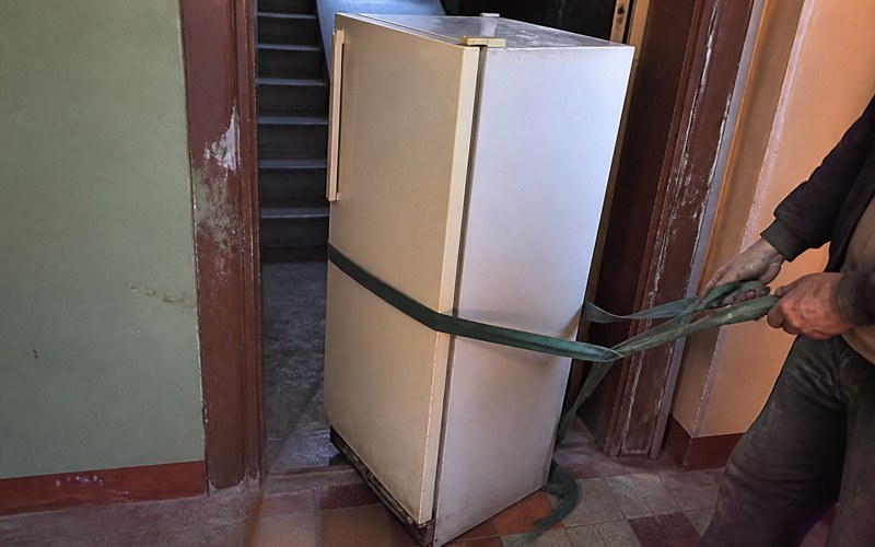 An old fridge with a carrying strap in a stairwell
