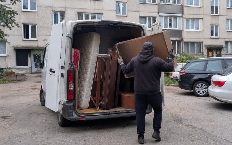 A worker loading old furniture into a van in a Riga courtyard